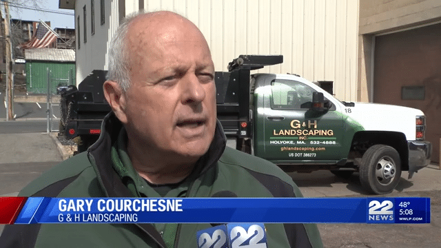 Gary Courches of G&H Landscaping speaks to 22 news in early April 2025 wearing a green parka and standing in front of the G&H Landscaping Inc., company truch which is white and green with yellow letters on the company logo. 