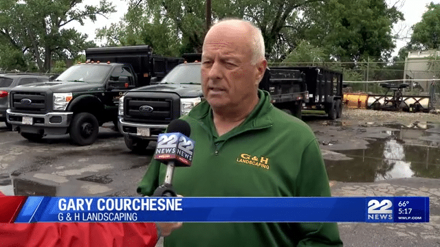 Gary Courches of G&H Landscaping speaks to 22 news in early April 2025 wearing a green parka and standing in front of the G&H Landscaping Inc., company truch which is white and green with yellow letters on the company logo. 